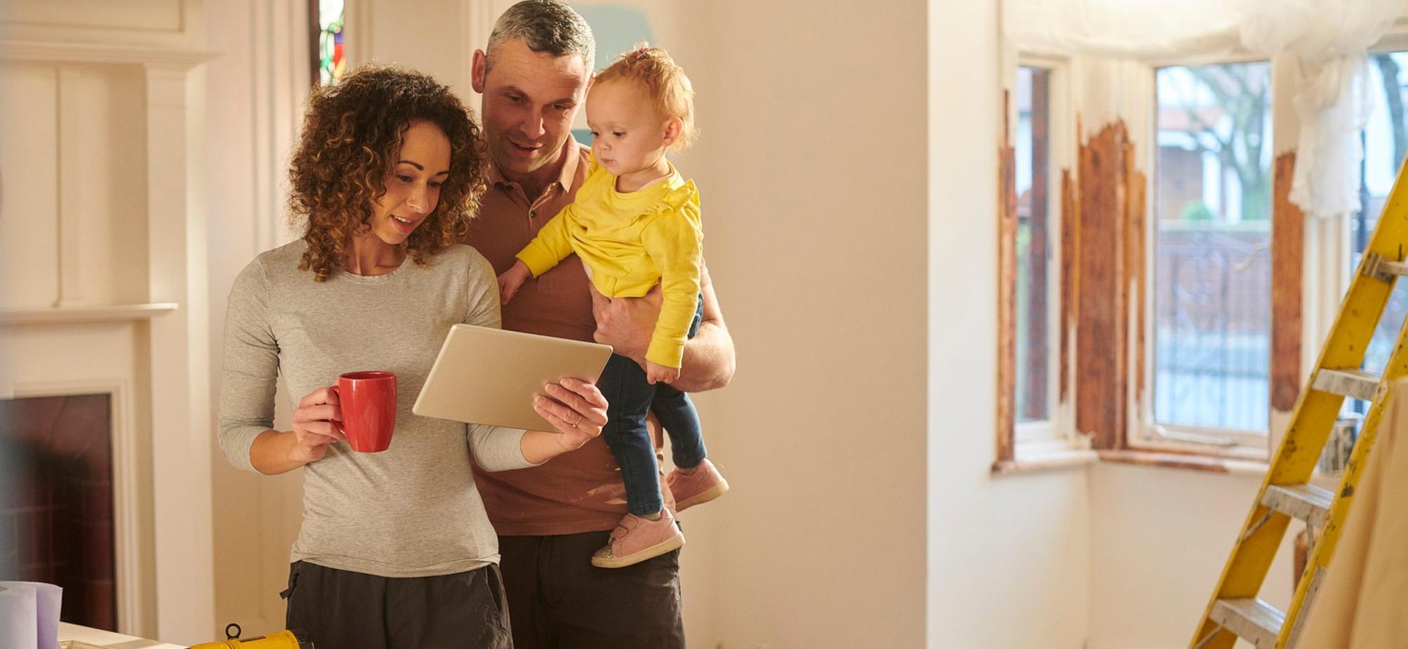 A picture of a couple, holding a baby, while reading instructions for doing home repairs